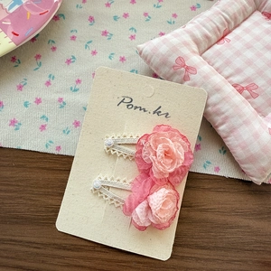Detailed view of pink chiffon flower hair clips with lace trim on a display card