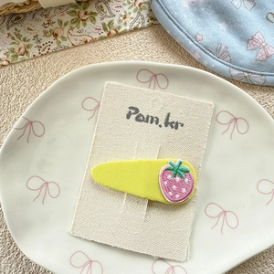 Detail of yellow fabric hair clip with strawberry embroidery on a canvas card