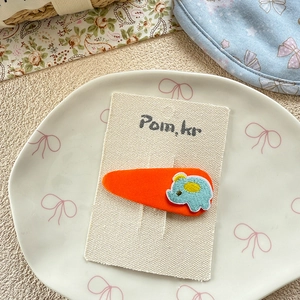 Detail of cute orange hair clip with embroidered blue elephant on a display card