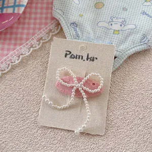 Detail einer Haarspange aus rosa Stoff mit einer Perlen-Schleife auf einer weißen Karte