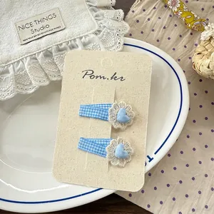 Détail de barrettes à carreaux bleus avec fleurs en dentelle beige et cœurs