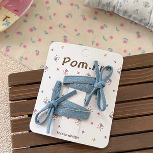 Detail of two denim blue bow hair clips on a white display card with floral patterns