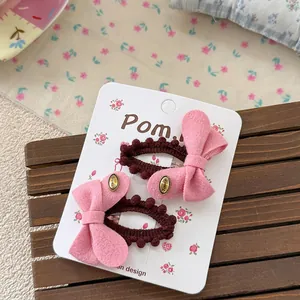 Detail of two pink bow hair clips with brown pom-pom edges on a floral card board