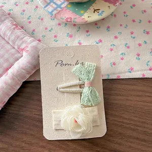 Detail of mint green lace bow and white tulle flower hair clips on a card