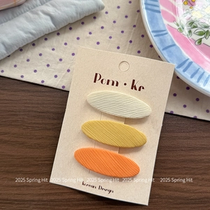 Set van drie stoffen haarspelden in crème, geel en oranje in Koreaanse stijl op een kaart