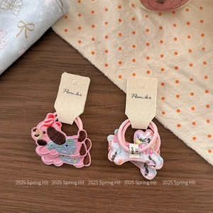 Detail of embroidered cat and bone hair ties with pink elastic bands on wooden surface