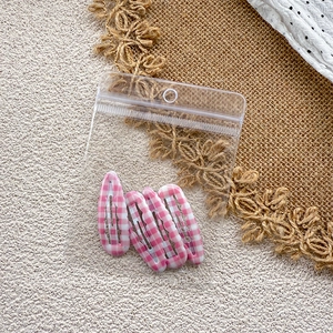 Close-up of four pink and white checkered resin BB hair clips in clear packaging