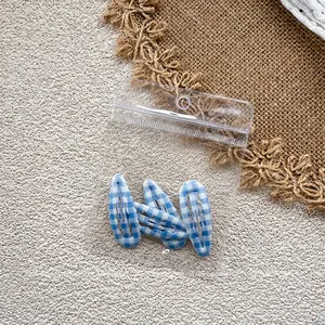 Close-up of three blue and white checkered hair clips in transparent plastic packaging