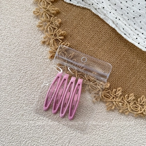 Detail showing set of four pink teardrop metal hair clips in transparent retail packaging