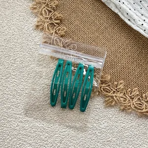 Close-up of four dark green teardrop metal hair clips in transparent packaging