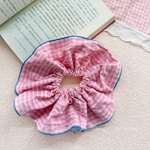 Close-up of pink checkered oversized scrunchie with blue stitched edges on white fabric