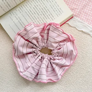 Detailed view of a pink striped oversized scrunchie on a beige textured background