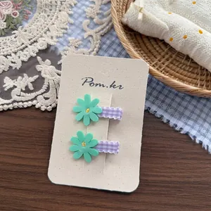 Close-up of daisy fabric hair clips with green petals and purple plaid base on display card