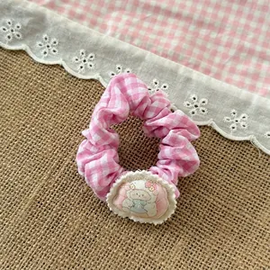 Close-up of pink checkered scrunchie with cute sheep patch on a rustic fabric background