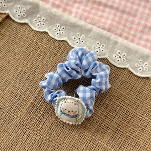 Detail of blue plaid scrunchie with a cute white cartoon cat charm on rustic linen