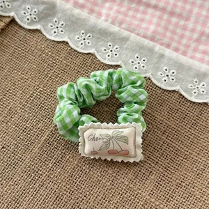 Detail of green plaid fabric scrunchie with cute cherry patch on a rustic backdrop