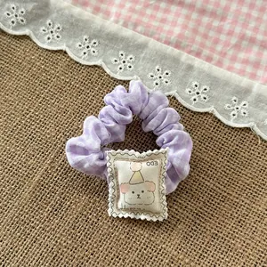 Close-up of purple plaid scrunchie with cute cartoon dog patch and happy text detail