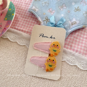 Détail de deux barrettes roses avec broderie de canard jaune sur support en carton
