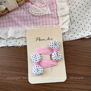 Detail view of two pink hair clips with blue polka dot fabric bows on card packaging