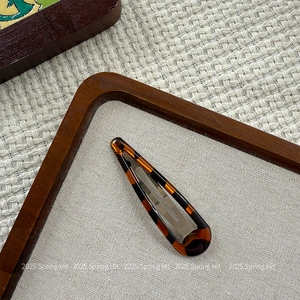 Macro shot of stylish tortoiseshell drop-shaped BB hair clip on textured fabric background
