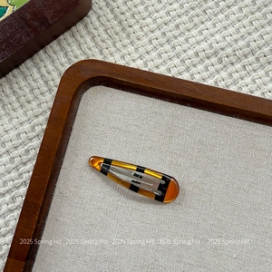 Detail view of a translucent amber tortoiseshell BB hair clip on a wooden tray