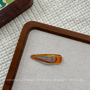 Close-up of a minimalist amber resin hair clip on a textured woven fabric background