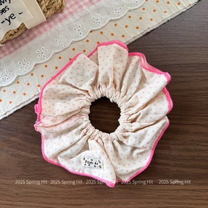 Close-up of a white scrunchie with pink dots and a woven label on a rustic background