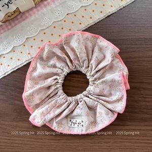 Close-up of pink floral scrunchie with delicate embroidery and Pom·kr brand label