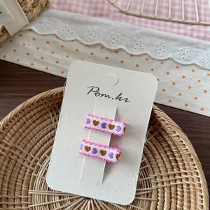 Dettaglio di fermagli per capelli con ricamo a cuore e pizzo rosa su cartoncino