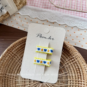Dettaglio di fermagli per capelli con cuore ricamato blu e giallo su carta marca