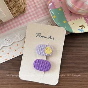 Détail de pinces à cheveux en tissu violet avec broderie canard jaune sur carte