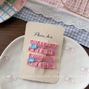 Close-up of pink plaid ruffle hair clips with blue gemstones and pink ribbon bows