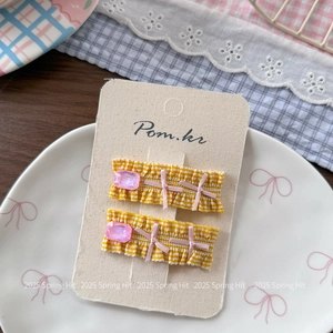 Close-up of yellow plaid hair clips with pink ribbon bows and faceted gems on card