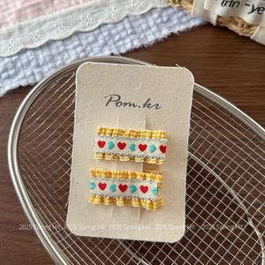 Close-up of yellow checkered fabric hair clips with red embroidered hearts for girls