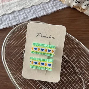 Detail of green gingham hair clips with embroidered heart pattern on display card