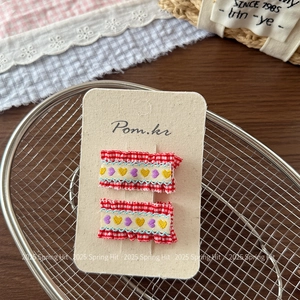 Close-up of red plaid fabric hair clips with embroidered hearts and ruffled edges