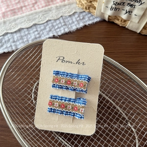 Close-up of handmade floral embroidery hair clips on blue checkered fabric base