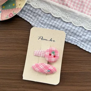 Pink checkered hair clips set with red cherry beads on vintage style ceramic plate