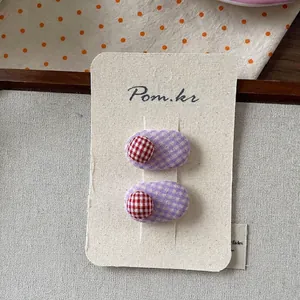 Detailed view of two checkered fabric hair clips in purple and red on a display card