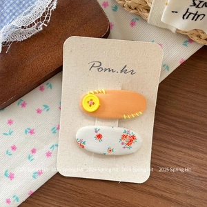 Détail des barrettes en tissu floral et de la pince orange avec bouton sur carte