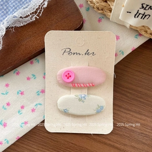 Détail de pinces à cheveux en tissu fleuri et bouton rose sur carte de présentation