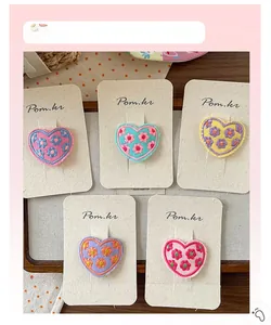 Detail of five colorful embroidered heart hair clips with floral patterns on a card
