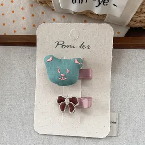 Détails des barrettes ours brodé et nœud marron sur carte de présentation