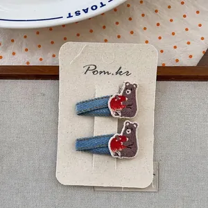 Détail de deux barrettes brodées d'ours faites à la main avec tissu denim bleu sur carte