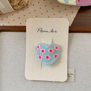 Detail of sweet heart-shaped embroidery hair clip with pink flowers on blue fabric base