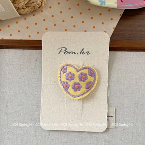 Detail of heart-shaped hair clip with yellow floral embroidery and purple petals