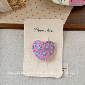 Close-up of pink heart-shaped embroidered hair clip with blue flower patterns on card