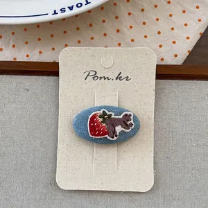 Détail de broderie faite main écureuil et fraise sur une barrette en jean bleu