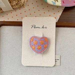 Close-up of purple heart-shaped hair clip with yellow floral embroidery on card