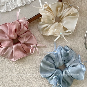 Close-up of three satin scrunchies in pink, champagne, and blue with bows and rhinestones